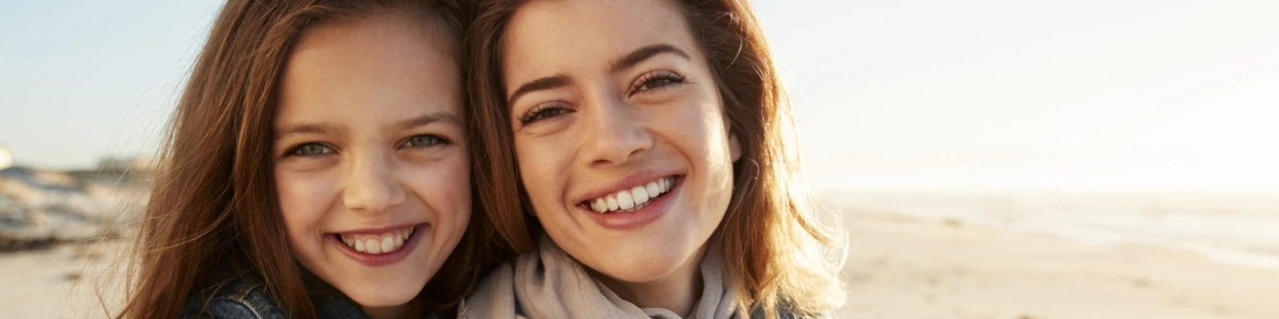 Two smiling women on a beach looking at the camera, sunny light