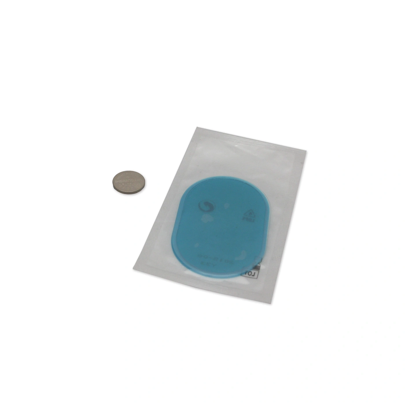 Una batteria a bottone accanto a un oggetto blu in una confezione.