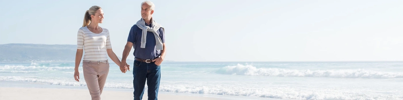 Couple walking on beach, holding hands, with ocean and sun in background