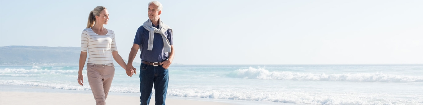 Couple walking on beach, holding hands, with ocean and sun in background