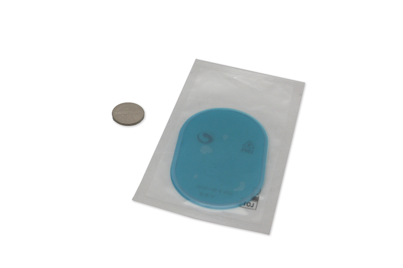 Oggetto blu in confezione accanto a una moneta su sfondo bianco.